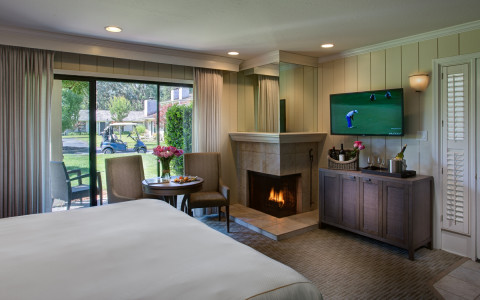 Mansion Junior suite bedroom with queen bed, mounted tv, lit fireplace and a private balcony overlooking the golf course