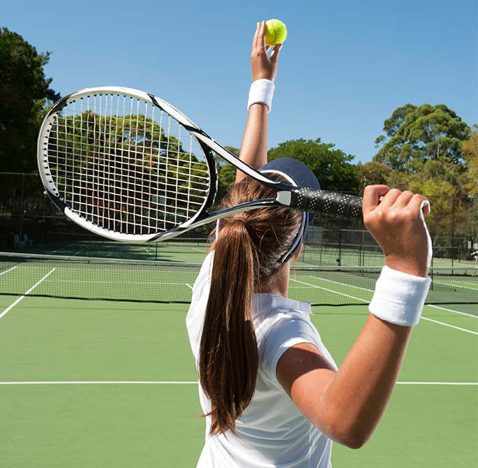 woman serving ball on a tennis field with trees at behind