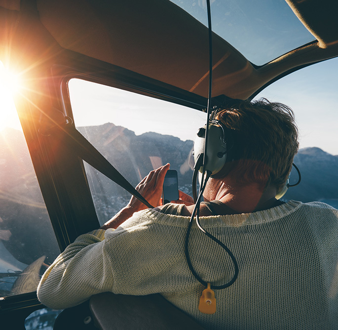 man in a helicopter taking pictures of the mountains at sunset