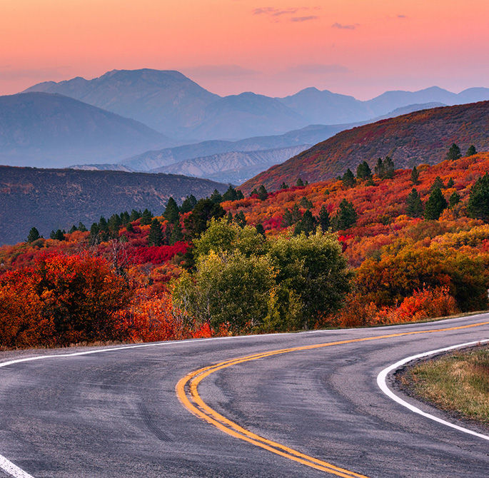 highway with mountains, green and red trees