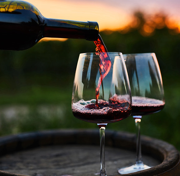 two glasses being filled with red wine during a sunset