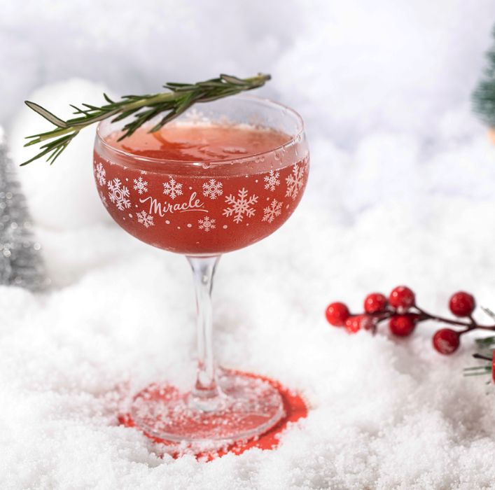 a cocktail glass with a snowflake design and a red drink inside of it sitting on a carpet of snow
