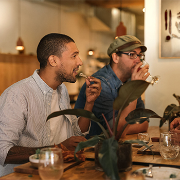 Two men eating and drinking lunch with plants