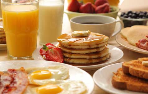 breakfast spread of pancakes, eggs, bacon, toast, OJ