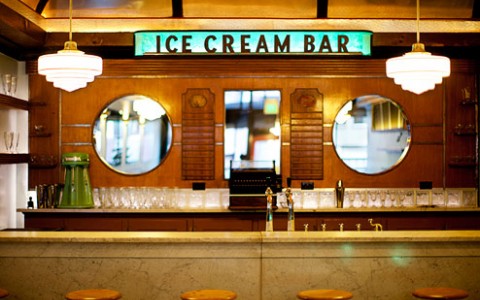 retro ice cream bar with stools up to a bar. glass cups line the back wall with a door into the kitchen.