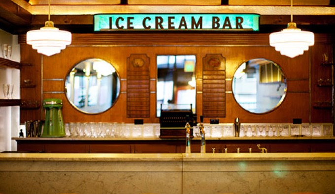 retro ice cream bar with stools up to a bar. glass cups line the back wall with a door into the kitchen.