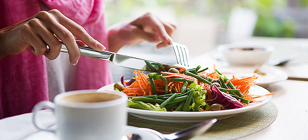 person preparing to eat salad at white cloth table