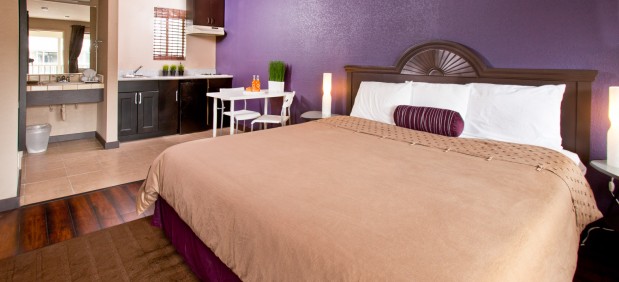 King sized bed in room with kitchenette and vibrant purple walls