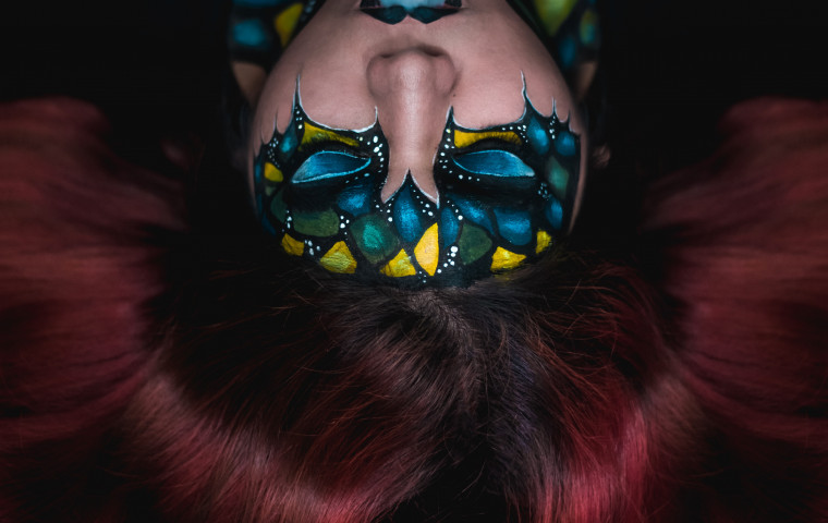 woman with burgundy hair lying down with face paint and blue smoke coming out of mouth