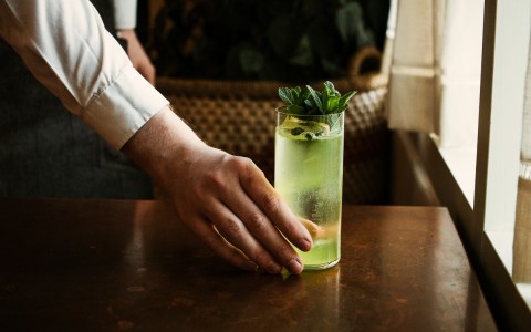 a hand holding a green cocktail on a table 