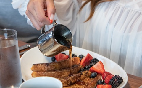 woman pouring syrup onto a plate of french toast