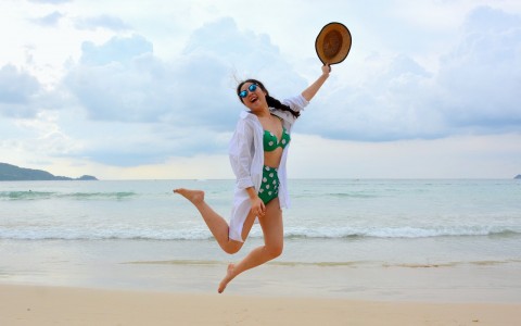 girl in bikini and shirt jumping on beach
