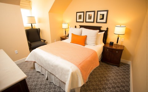 bedroom with dark furniture and orange accents on the bed and a chair next to the bed 