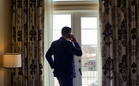 a man in a suit while holding a phone to his ear and looking out the window 