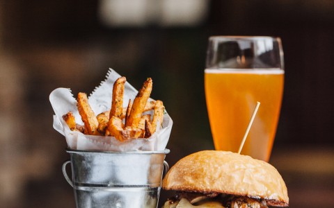 plate of burger and fries with a beer in the background sitting on a white table 
