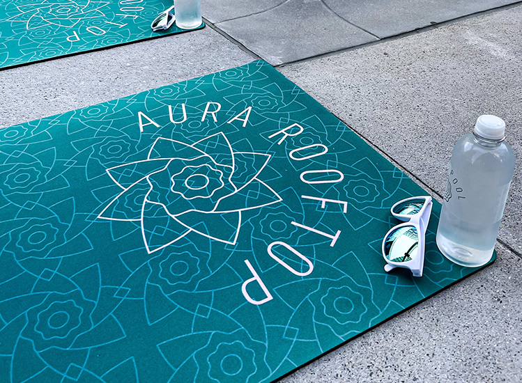 yoga mat that reads aura rooftop with sun glasses and water bottle next to it