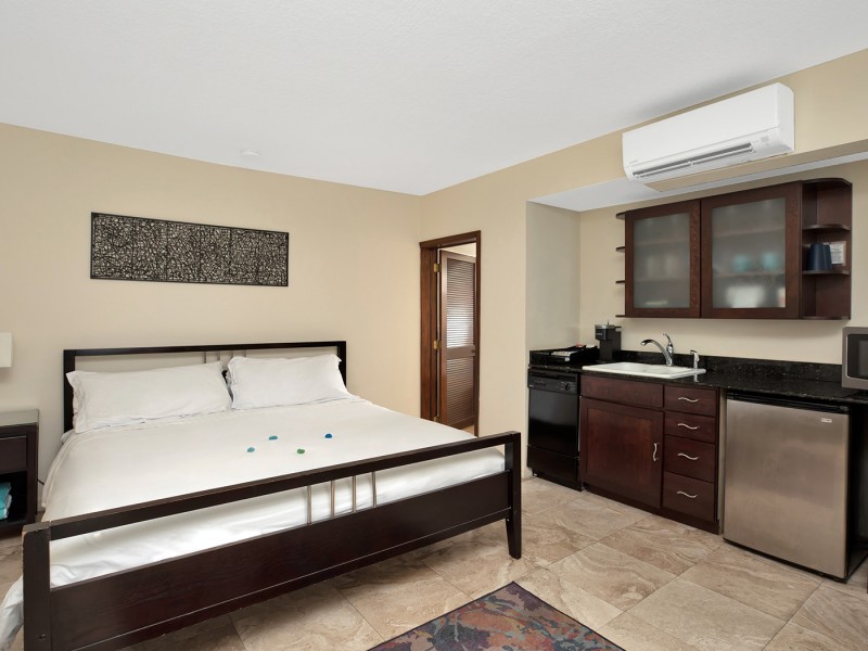 white linen bed with mini kitchen on left side with sink, microwave, and fridge and cabinet above