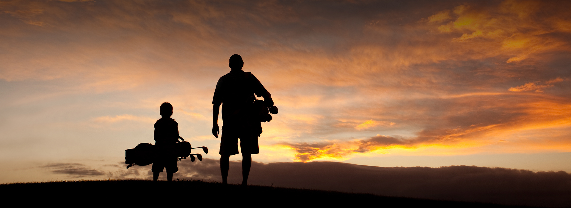 View of a father and his son carrying some golf sticks at sunset 