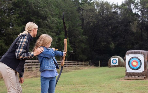 a woman and a young girl doing archery
