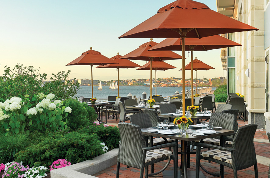outdoor dining area with orange umbrellas and flowers overlooking the water
