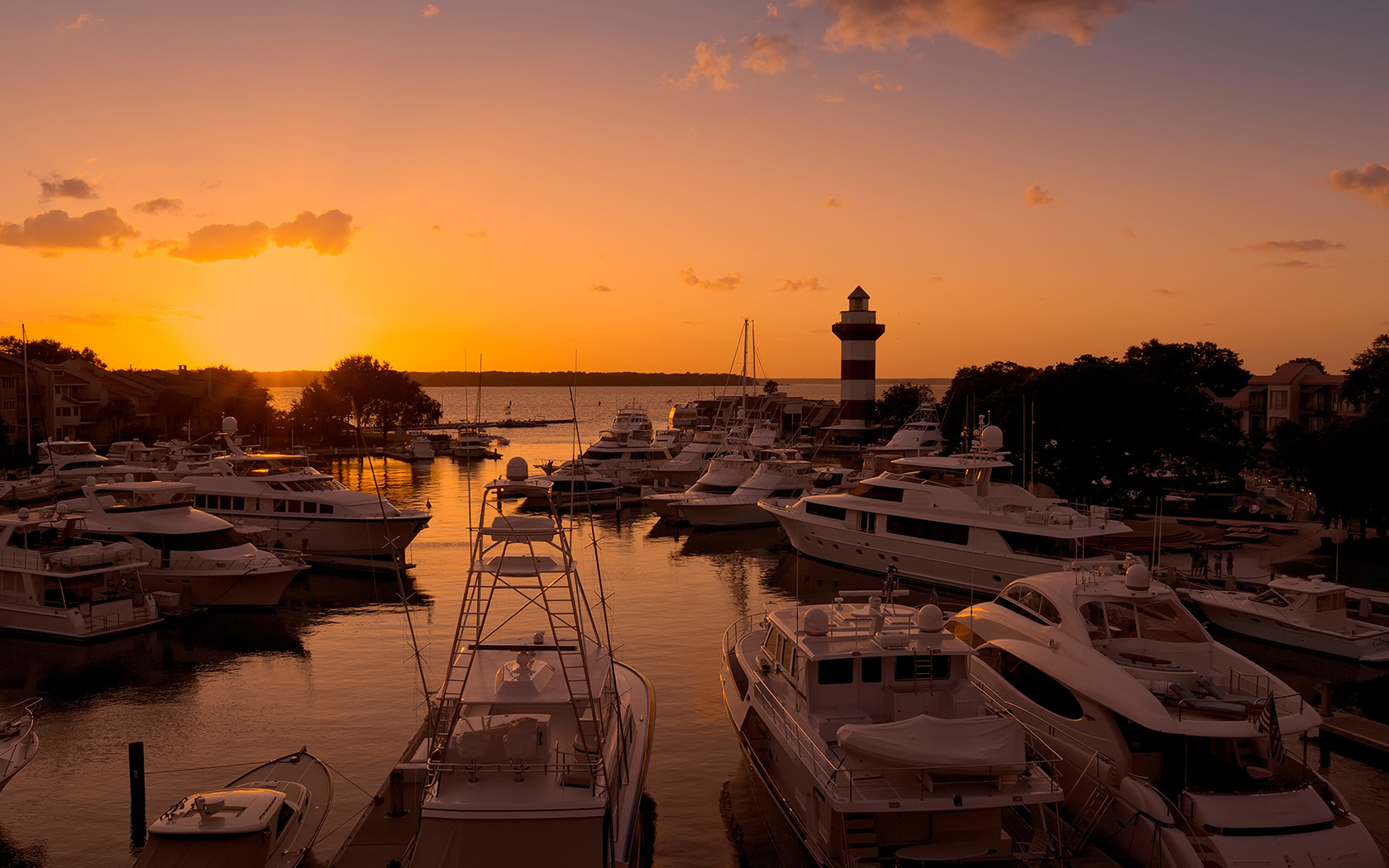a marina with boats and a lighthouse as the sun sets in the distance
