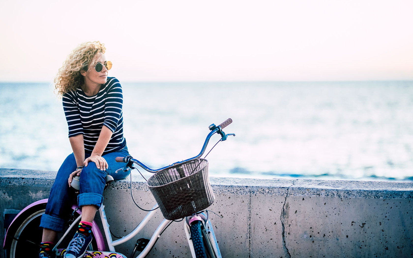 a woman with her bicycle sitting on a concrete ledge with the ocean in the distance