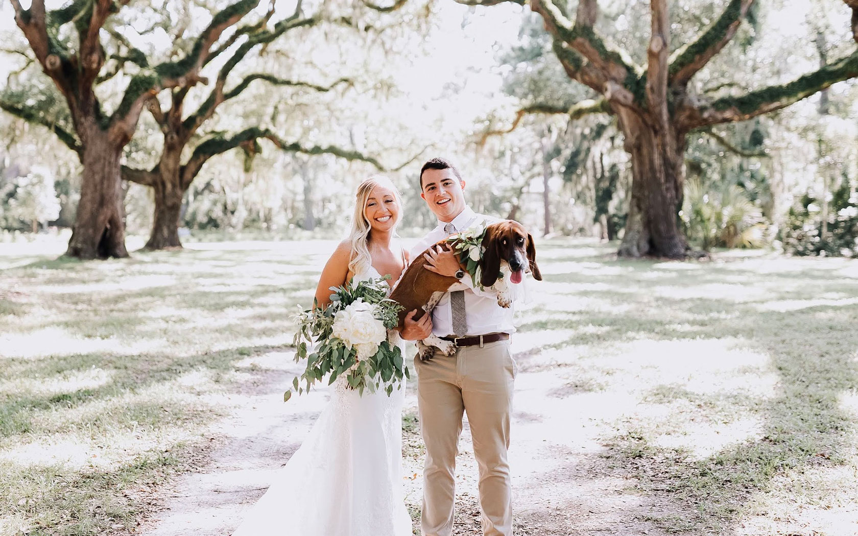 a smiling bride and groom posing for a picture while holding a dog 