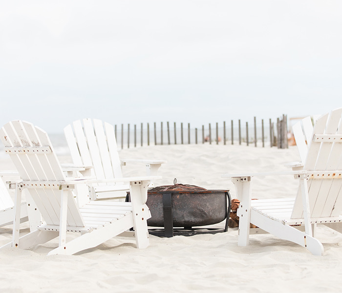 white adirondeck chairs on the beach with a fire pit in the middle
