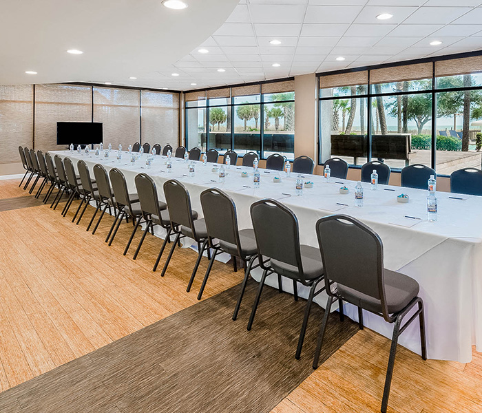 a long white table set up for a meeting with a television against the wall