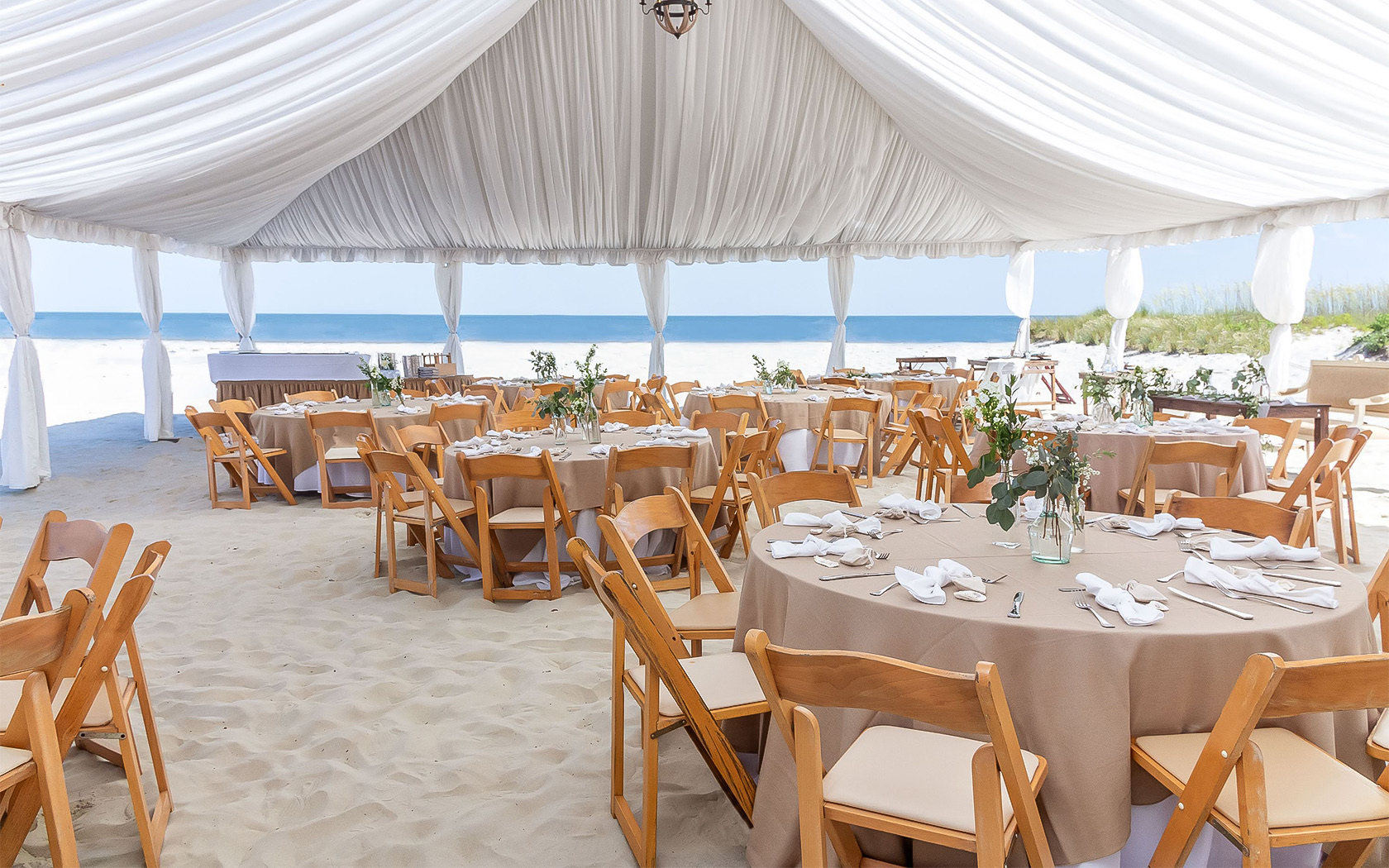 a large white tent with tables and an outdoor bar and the ocean in the distance