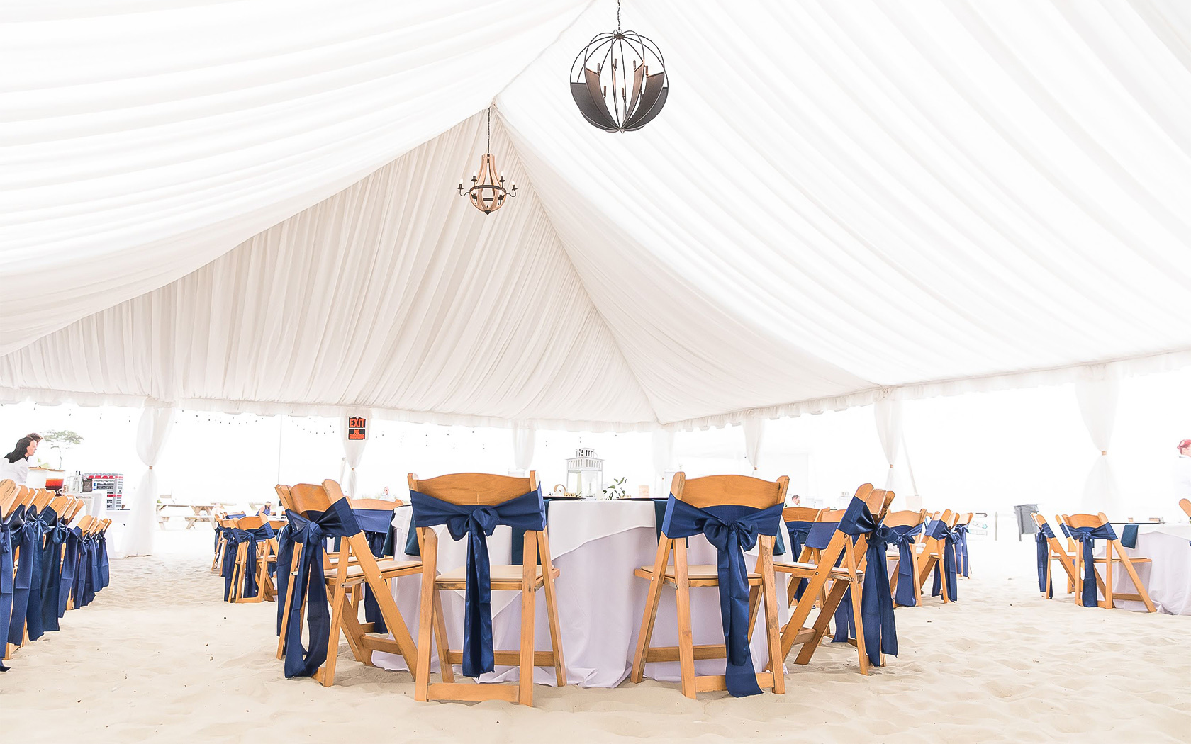 an outdoor tent with chandeliers hanging from the ceiling and chairs wrapped with navy blue ribbon