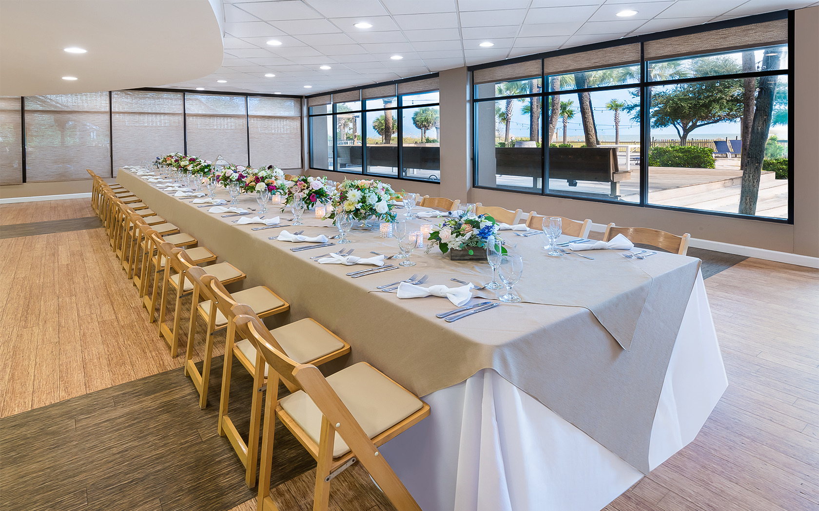 a long rectangle shaped table with wooden chairs and many floral centerpieces