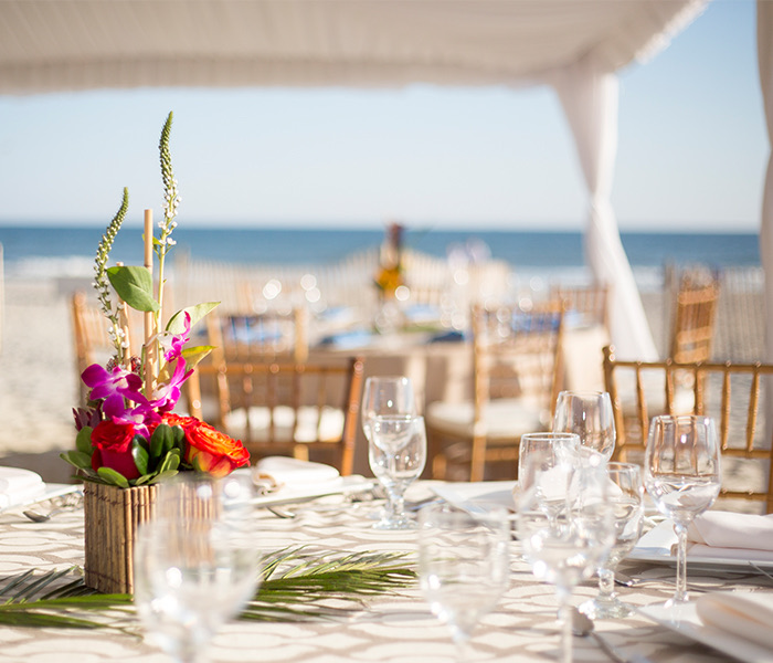 close up of a table under a tent with a tropical centerpiece in the middle and the ocean in the distance
