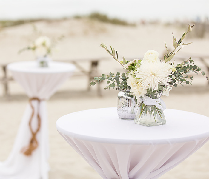 close up of a high top with white linen on top and two small floral centerpieces