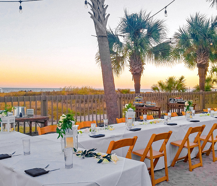 a t-shaped table set up for an event on the beach at sunset