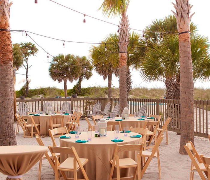 small round tables with light brown linen on the beach with palm trees