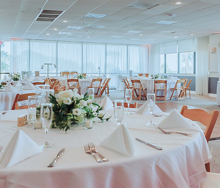 a close up of a white linen covered table with a white floral centerpiece and lots of natural light