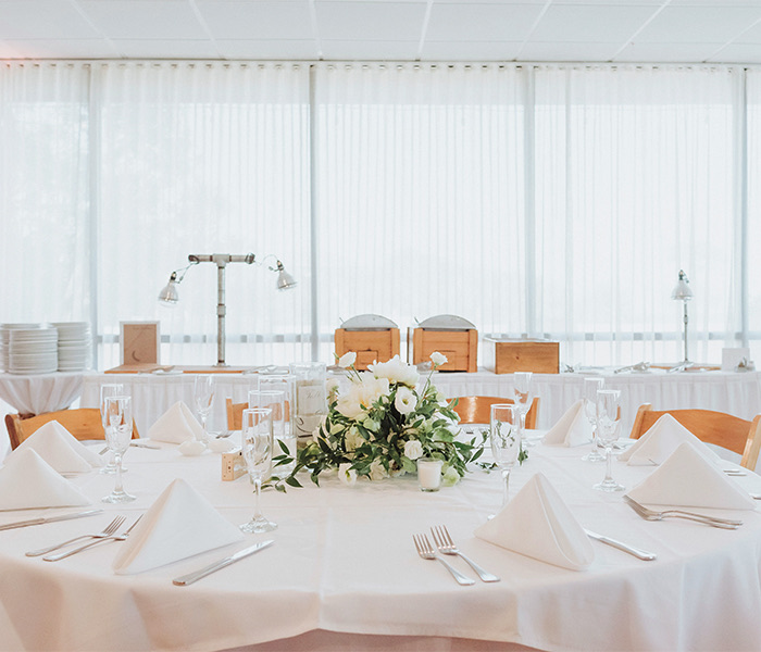 a large white linen covered table with light brown chairs and a white floral centerpiece in the middle