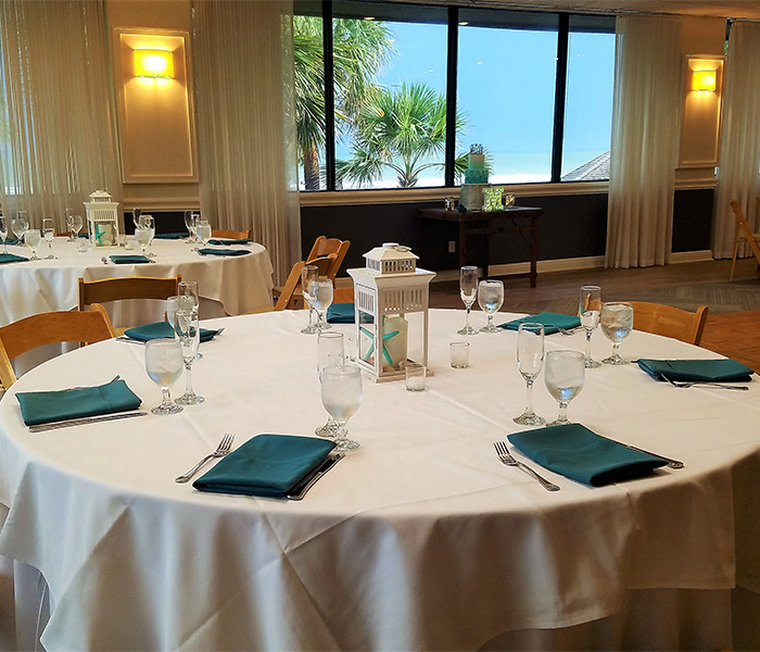 a large white table with teal dinner napkins and a lantern in the middle