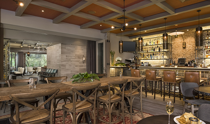 Rustic indoor dining space with wooden tables & chairs next to bar stocked with liquor