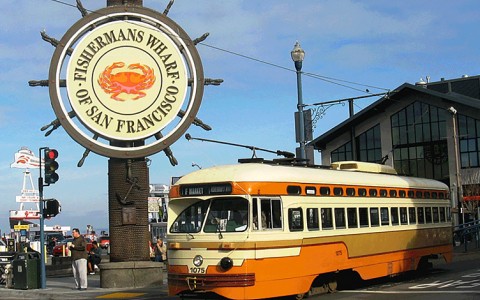 a boat wheel themed sign for the Fishermans Wharf of San Francisco and an old fashioned orange, brown and cream bus