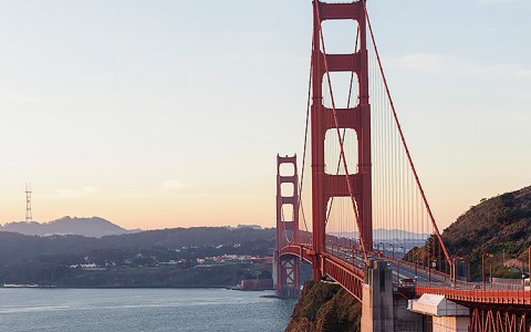 Red Golden Gate Bridge over a body of water with orange and blue sunset in background