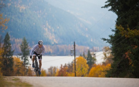 Man Bicycling on Street Wearing Helmet with Lake and Mountains in Background