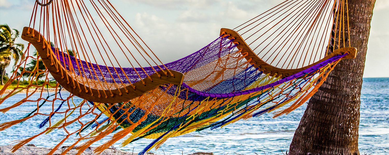 an empty colorful hammock hanging between two palm trees on the beach