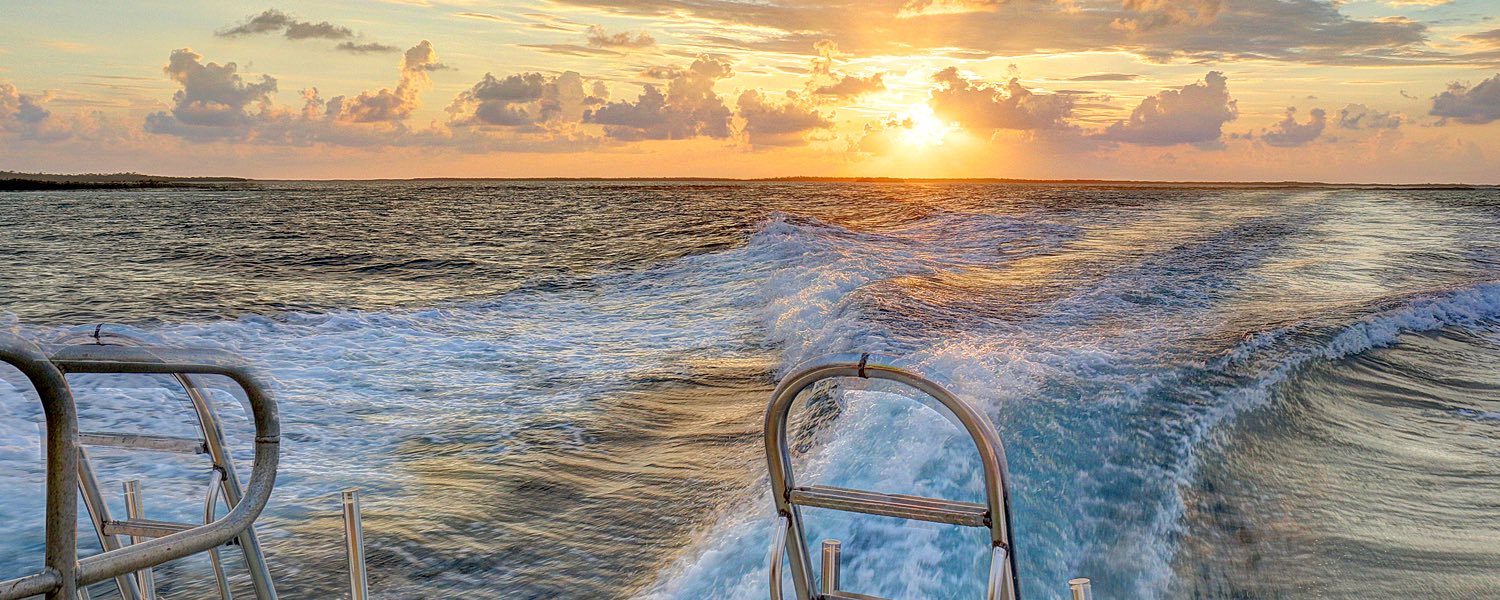 a view of the sun setting over the ocean seen from behind a boat diving in the water