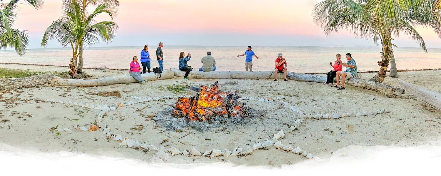 group of friends sitting around a beach bonfire at sunset