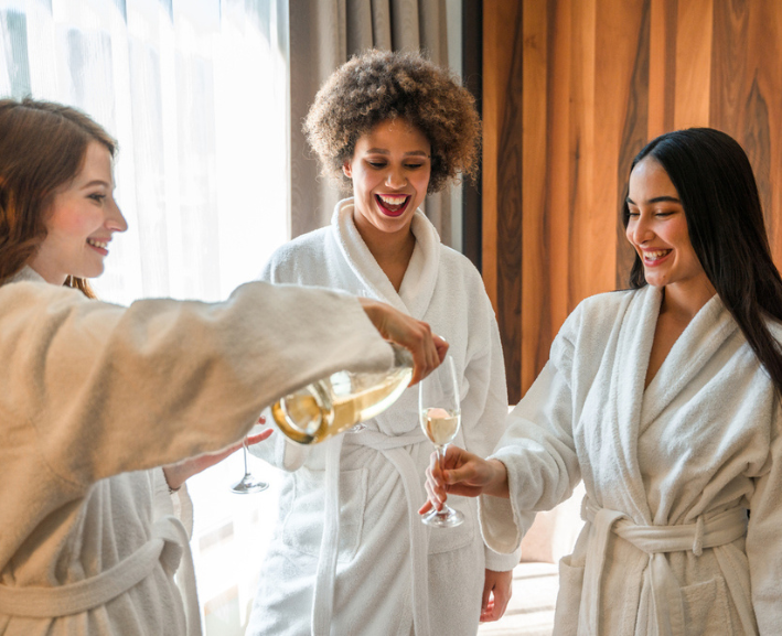 Three women wearing white spa robes while drinking champagne