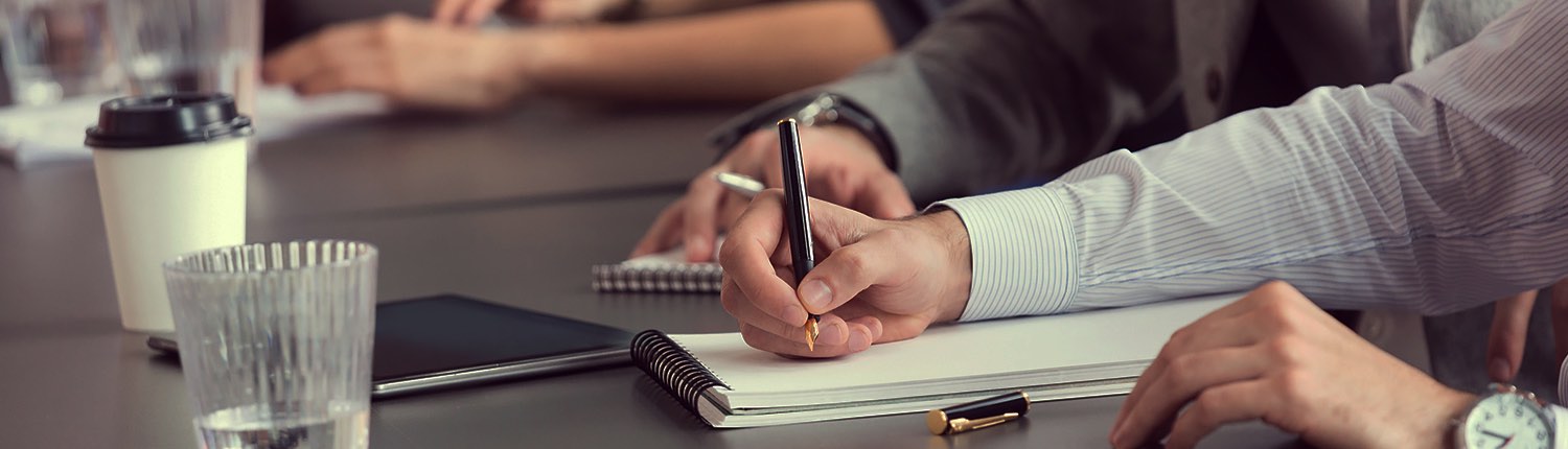 close up of a business man taking notes on a pad of paper at a meeting