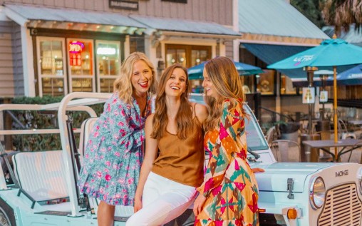 3 smiling women hanging out during the evening and a summer turquoise  blue car 