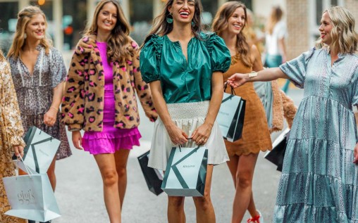 6 happy young women walking in the street holding small sized shopping bags